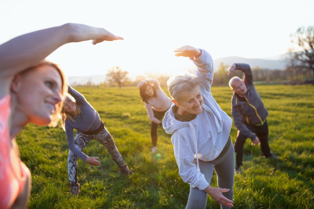 Seniors with sport instructor doing exercise outdoors in nature at sunset, active lifestyle.