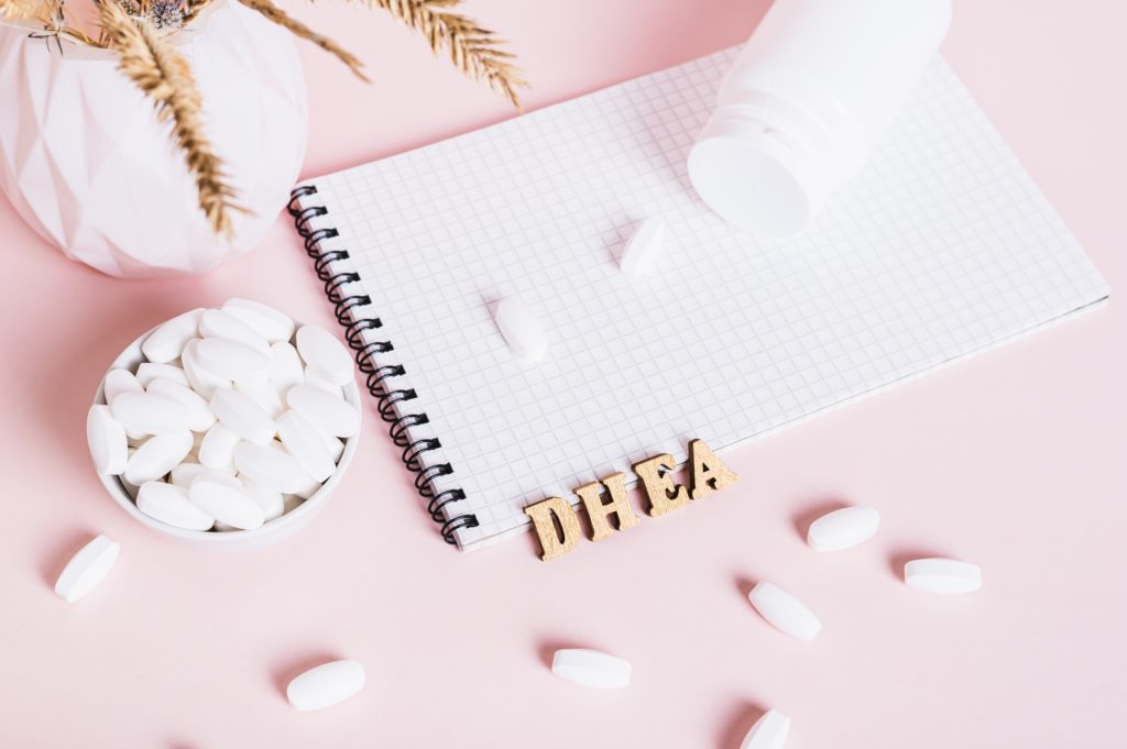 Hormonal supplements in a bowl, notebook and bottle on pink background