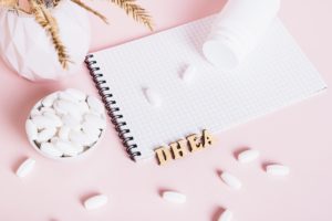 Hormonal supplements in a bowl, notebook and bottle on pink background